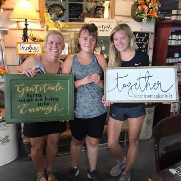 Meg posing between two Edgy Meg's art class participants both holding custom signs.